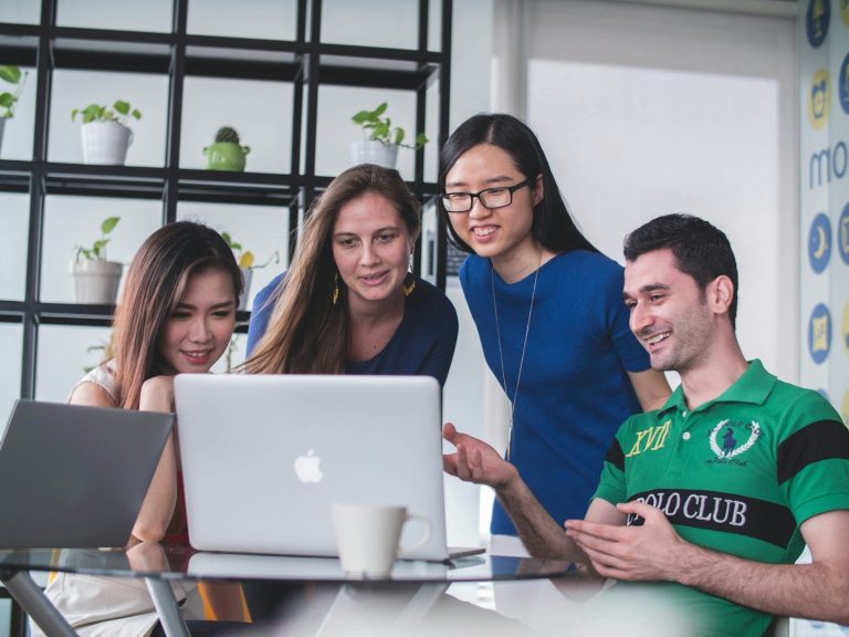Three woman and a man at a computer, Three woman and man looking at one computer screen smiling